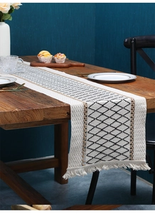 Detail of woven table runner with diamond pattern and white fringe on wooden table
