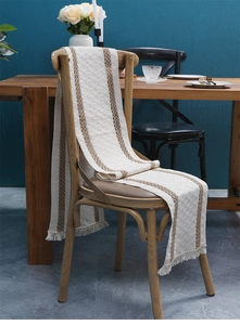 Detail of woven table runner with diamond pattern and fringes on a wooden chair