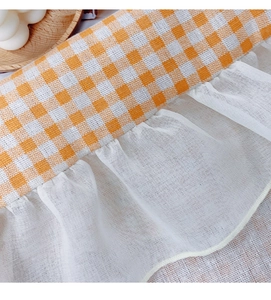 Close-up of orange and white checkered tablecloth with delicate white lace ruffle edges