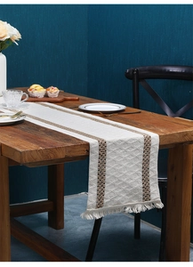 Detail of bohemian cotton linen table runner with woven tassels on a dark wood table