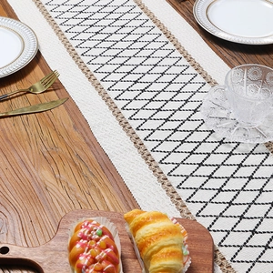 Modern black and white geometric woven table runner with rustic jute edges on wooden table