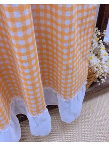 Detail of orange and white gingham fabric with white translucent ruffle lace hem