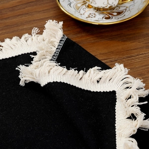 Minimalist black woven placemat with cream tassel fringe on dark wood table