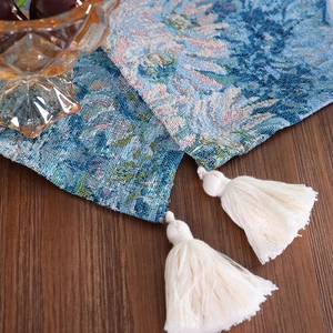 Blue floral jacquard table runner with white cotton tassels on a brown wooden table