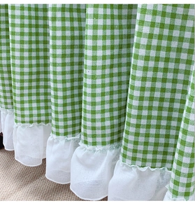 Detail of green plaid cafe curtain featuring delicate white lace ruffle hem and textured fabric