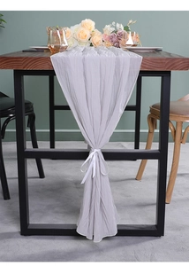 Detail van lichtgrijze geplooide tafelloper met wit lint aan houten tafelrand decor