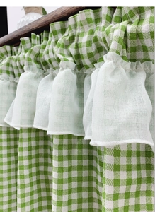 Detail of green plaid cafe curtain with white ruffled trim on a wooden rod