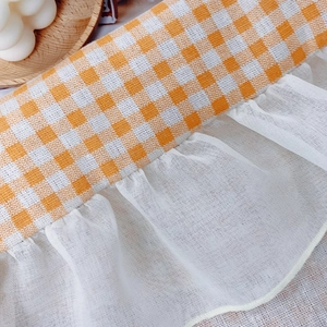 Orange gingham plaid tablecloth with white lace edges in a cozy minimalist home setting