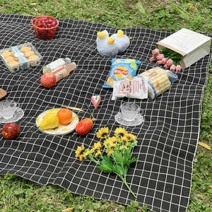 Portable black and white checkered picnic mat on green lawn with outdoor dining snacks
