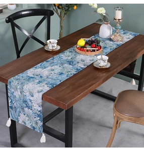 Detail of blue floral jacquard table runner with white tassels on dark wood table