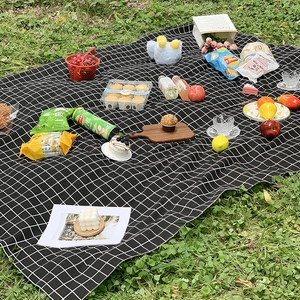 Portable black and white checkered picnic mat spread on green grass for outdoor camping