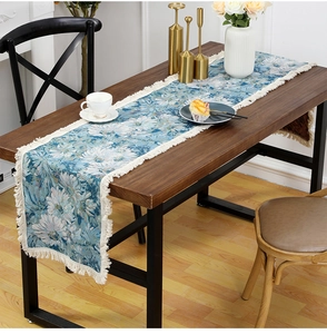Floral table runner with white daisies and fringe tassels on a dark wood table surface