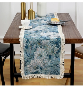 Detailed view of teal floral table runner with elegant cream tassels on wooden surface