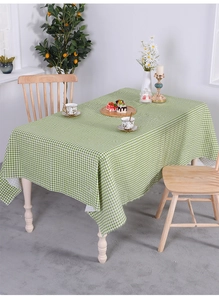 Detail of green and white checkered cotton linen tablecloth with fringe edges on wood table