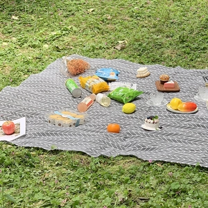 Outdoor portable picnic mat with gray leaf pattern spread on green grass for camping