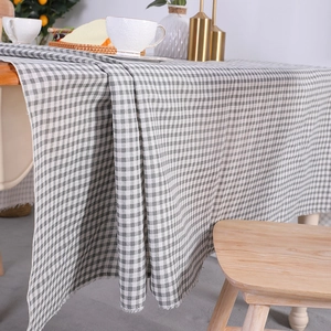 Grey and white checkered linen tablecloth with decorative tassel fringe on a wooden table