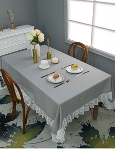 Detail of grey linen tablecloth featuring elegant white wide lace edge in a cozy home setting