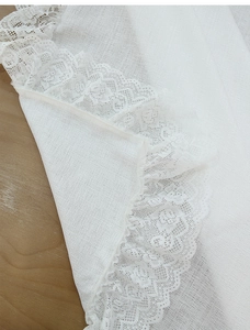 Detailed close-up of delicate white lace trim on a Nordic minimalist linen-textured tablecloth