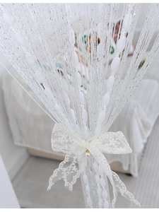 Close-up of white tassel fringe curtain with oval beads and decorative lace bow tied in center