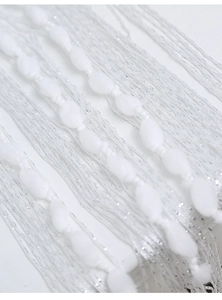 Macro shot of white string curtain with translucent oval beads and metallic shimmer