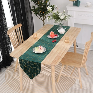 Détail d'un chemin de table vert foncé avec motifs géométriques dorés et pompons blancs