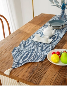 Detail of blue cotton linen table runner with white leaf patterns and fringe tassels