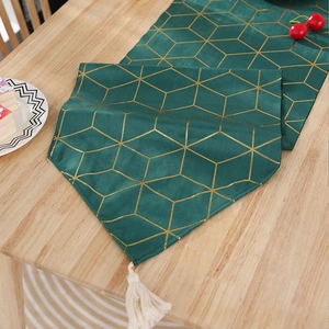 Détail d'un chemin de table en velours vert avec motifs dorés et glands blancs