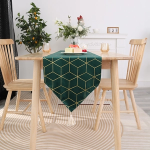 Détail d'un chemin de table vert foncé avec motifs dorés et pompons blancs décoratifs