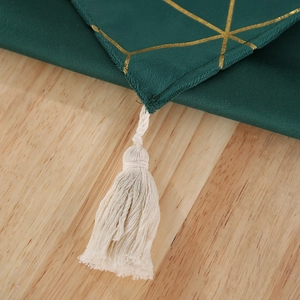 Détail d'un chemin de table vert foncé avec motifs dorés et pompons crème élégants