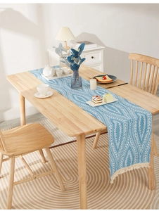 Close-up of light blue cotton linen table runner with white leaf patterns and tassels