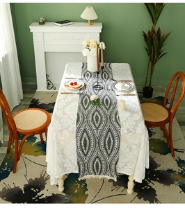Detail view of modern leaf pattern table runner with tassels on white lace tablecloth