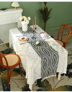 Detail of bohemian table runner with tassels over white damask lace tablecloth