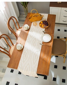 Detail of beige table runner with white leaf pattern and tassels on a wooden dining table