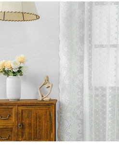 Dettaglio della tenda in pizzo bianco con motivi floreali vintage e bordi a onde