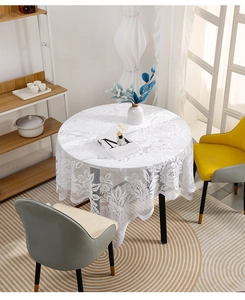 Detail of white lace tablecloth with floral embroidery and wavy edges on a round wooden table