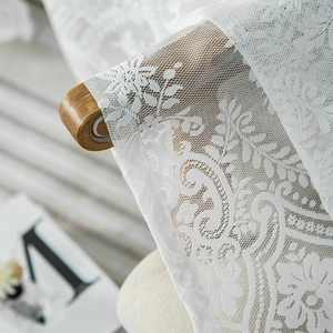 Elegante tenda in pizzo bianco con motivi floreali drappeggiata su una sedia in legno
