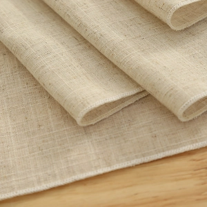 Minimalist beige polyester table mat with durable hemmed edges on a wooden surface