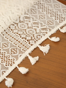 Macro view of vintage beige crochet table runner with hollow lace and fringe detail