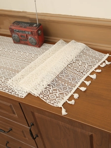 Detail of white hollow crochet table runner with intricate floral patterns and fringe