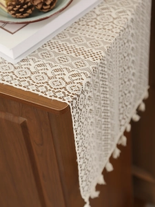 Detailed close-up of white crochet lace table runner with floral texture and fringe tassels