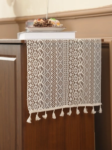 Detail of vintage beige lace table runner with hollow crochet floral patterns and tassels