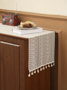 Detailed close-up of white crochet table runner with floral hollow patterns and fringe