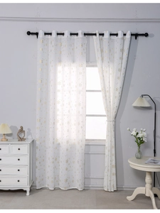 Close-up of white sheer curtains with gold foil snowflake patterns and metal grommets