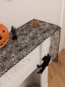 Detail of Halloween spider web lace table runner on mantel with pumpkins and bats