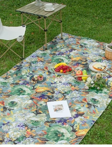 Detailed view of vintage oil painting style picnic mat with floral pattern on green grass