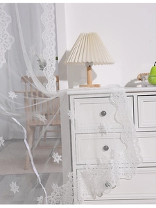 Detail of white lace sheer curtain featuring elegant floral embroidery and scalloped edges