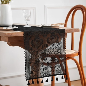 Close-up of black lace table runner with intricate hollowed patterns and fringe tassels