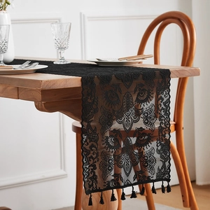 Close-up of black floral lace table runner with delicate tassels on a wooden dining table