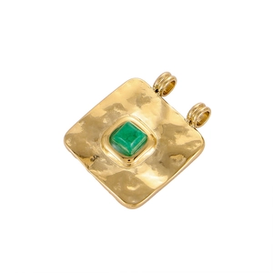 Detailed macro view of gold-plated square pendant with green gemstone and hammered finish