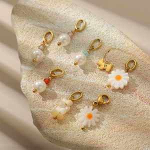Handmade freshwater pearl earrings with daisy charms and golden animal pendants on stone